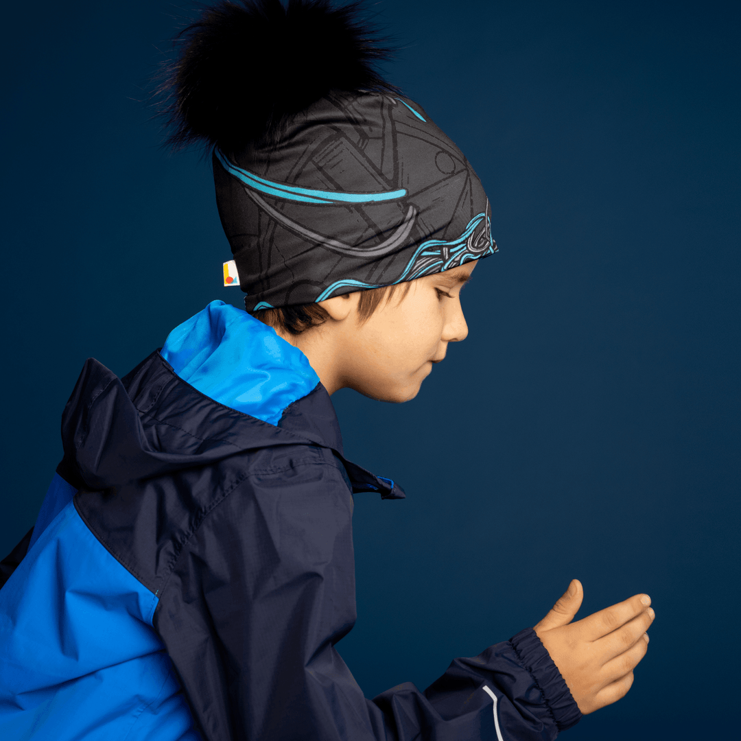 Side profile of a young boy wearing the black and blue patterned Robocats Beanie and a blue jacket, with his head bowed and hands near his chest.