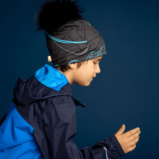 Side profile of a young boy wearing the black and blue patterned Robocats Beanie and a blue jacket, with his head bowed and hands near his chest.