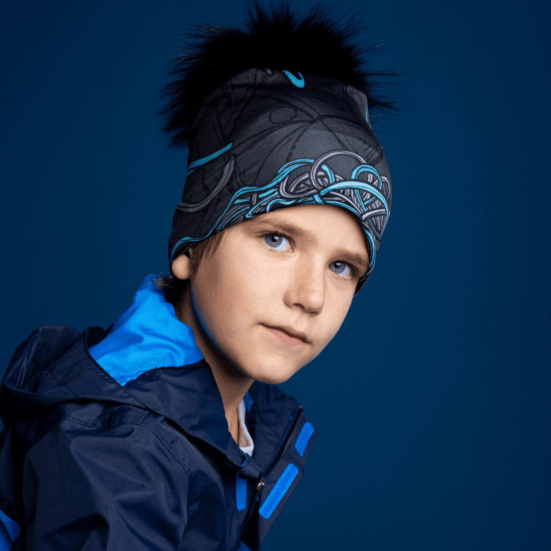 Profile view of a young boy wearing the black and blue patterned Robocats Beanie and a blue jacket, looking downwards with his head tilted.