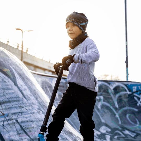 Young boy with a scooter in a skatepark, wearing the Robocats print beanie and neck warmer.