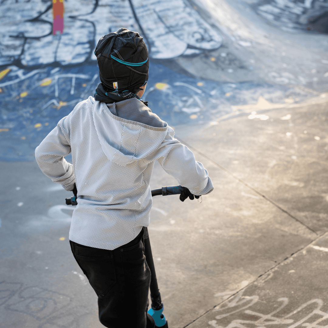 View from behind of a boy on a scooter in a skatepark, wearing the Robocats beanie and neck warmer.