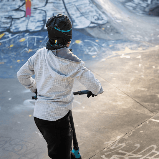 View from behind of a boy on a scooter in a skatepark, wearing the Robocats beanie and neck warmer.