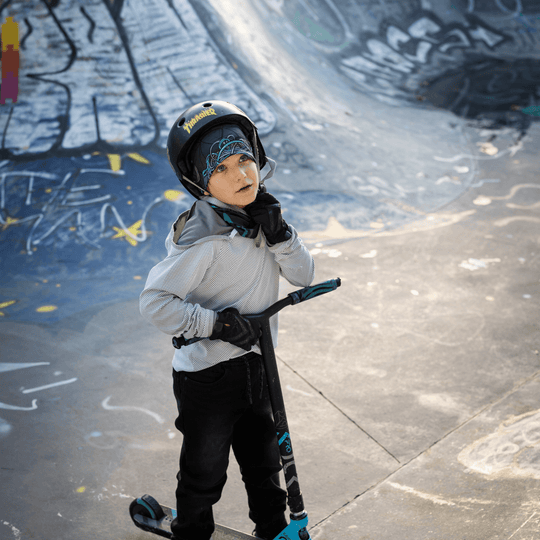 Close-up of a young boy in a skatepark, wearing a helmet over the Robocats Black and Blue Beanie and neck warmer.