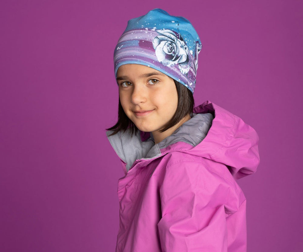 A young girl in a pink jacket wearing the blue floral Roses Beanie.