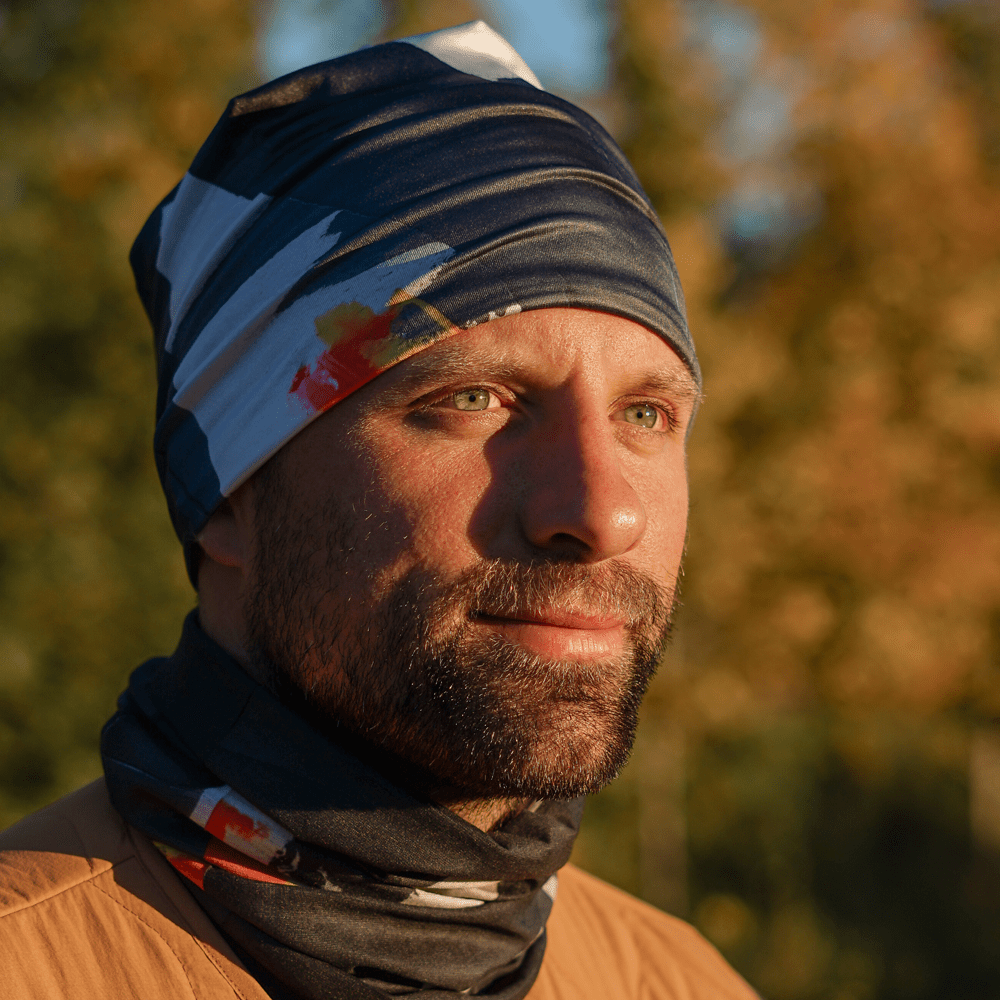 Man wearing a multi-colored abstract art neck gaiter and matching beanie outdoors.