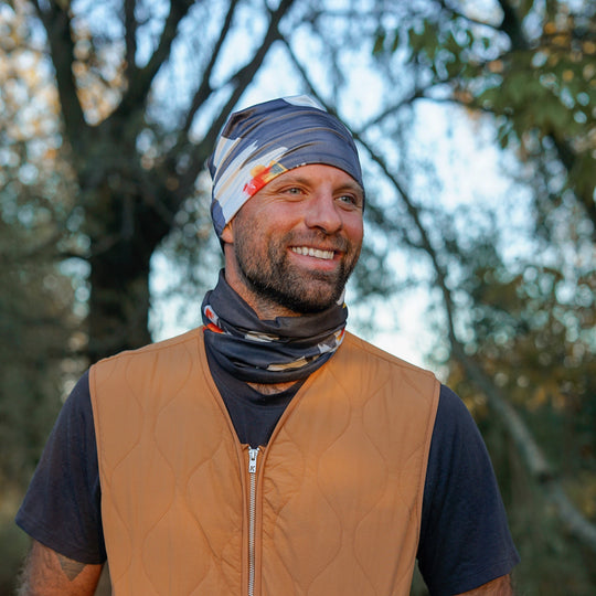 Man wearing a bandana tube as a headband and neck gaiter, smiling outdoors.