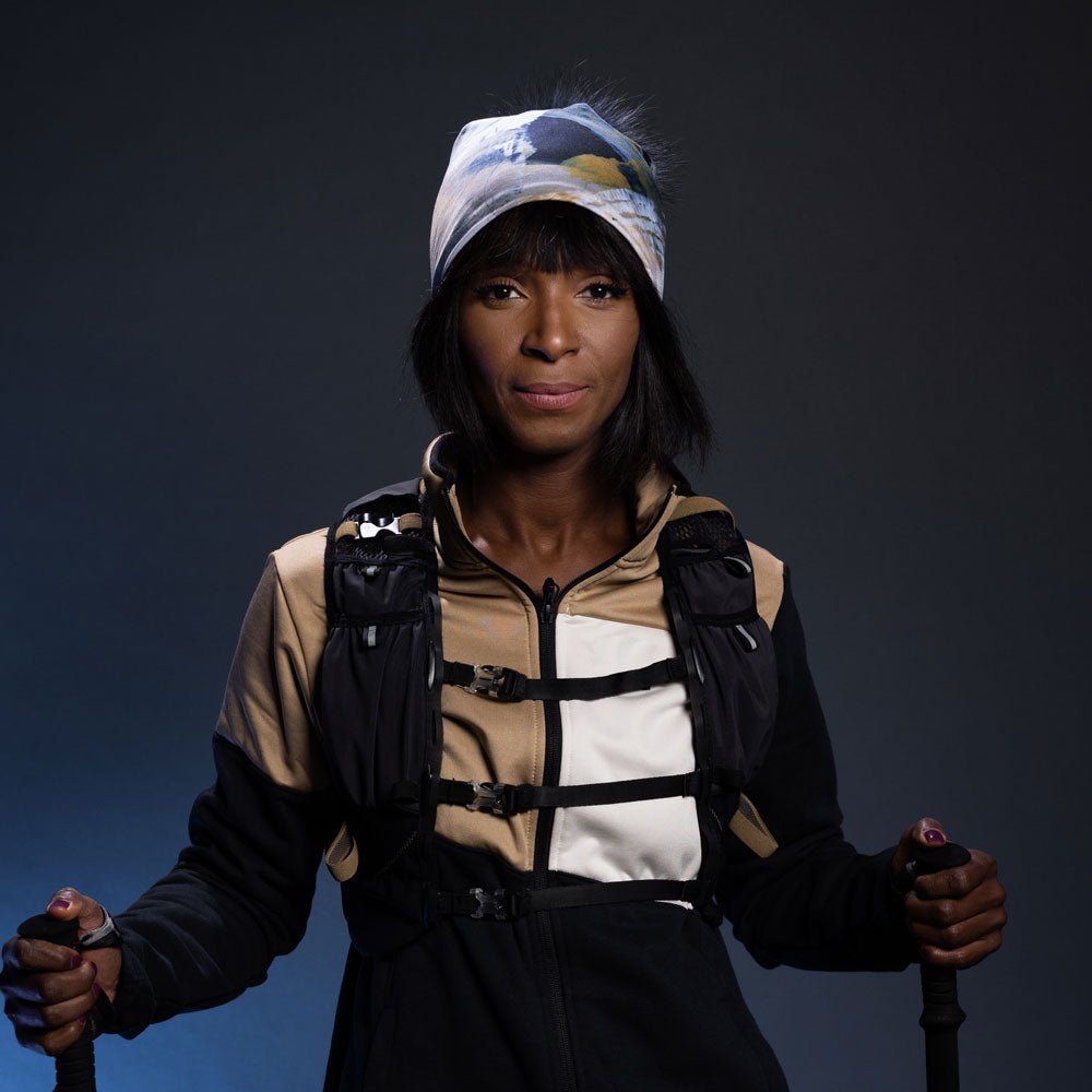 Woman wearing the Sand Beanie with Black Removable Pompom and a hiking vest, holding trekking poles