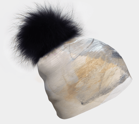 Beige, white, and black abstract print beanie with a large black fluffy pom-pom