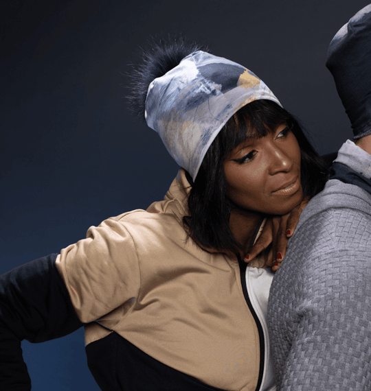 Close-up of two people wearing beanies with abstract prints and removable pompoms