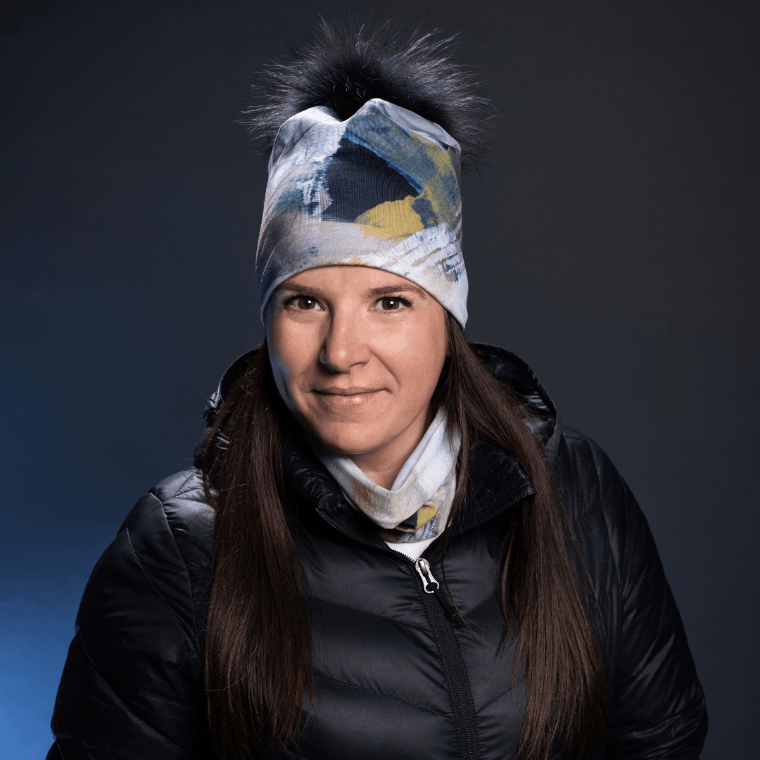 Woman wearing the Sand Beanie with Black Removable Pompom, smiling, against a dark background
