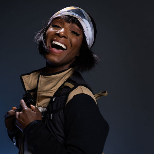 A person wearing the Sand Multifunctional Tube as a headband with a bright smile and a backpack.