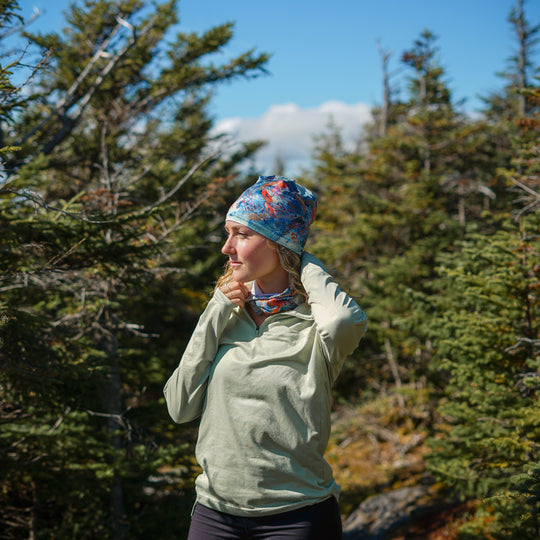 Woman wearing the Sphénédon Beanie and matching neck gaiter while hiking in a forest.