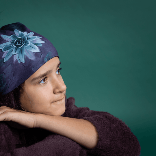 Young girl with dark hair wearing the Succulent Beanie and a fuzzy dark purple sweater, looking thoughtfully to the side against a teal background.