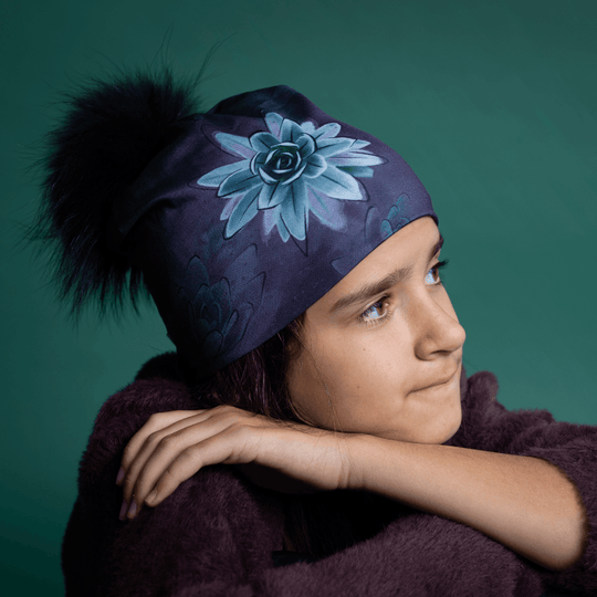 Side profile of woman wearing deep navy succulent art beanie with black pompom, showcasing bold teal botanical print detail