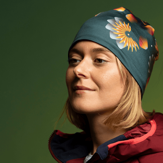 Woman wearing a dark green beanie with a floral print, smiling against a green background.
