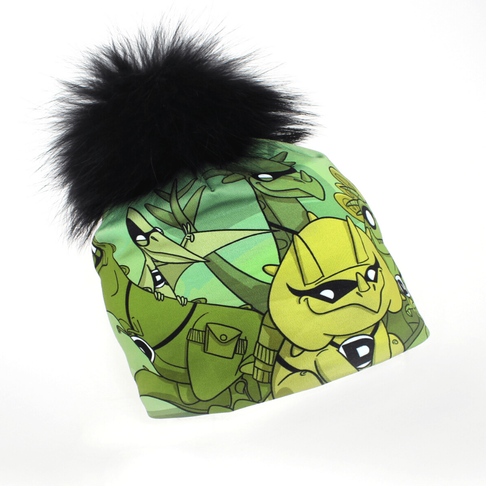 Green beanie with a black fluffy pompom, decorated with illustrations of cartoon dinosaurs.