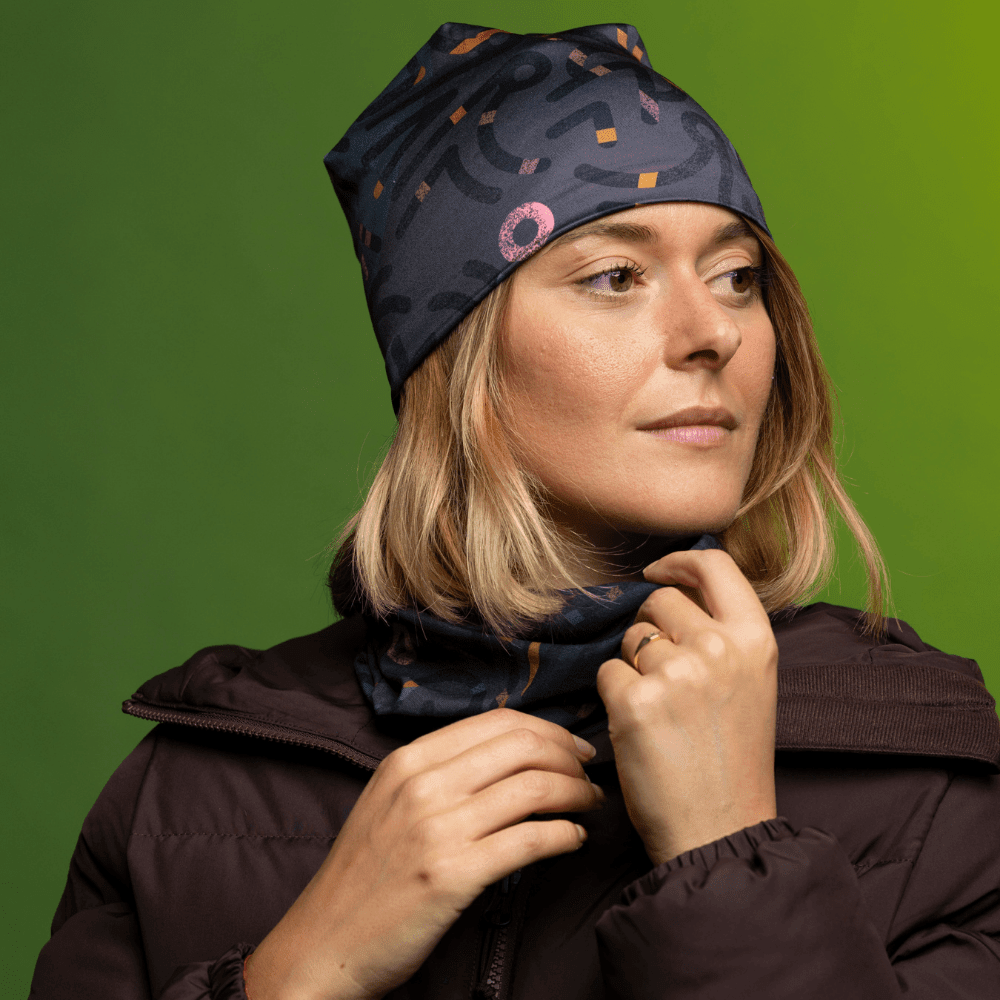 Woman wearing a dark brown puffer jacket, a gray beanie with abstract pattern, and a matching neck gaiter.