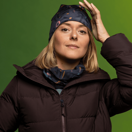 Woman wearing a dark brown puffer jacket, touching her gray beanie with an abstract pattern.