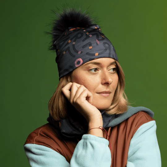 Woman wearing a gray beanie with a black pompom and matching neck gaiter, looking off to the side.