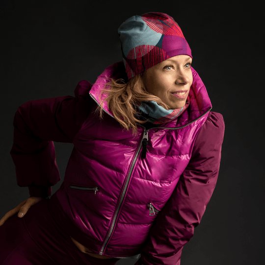 Woman in a purple ski jacket and leggings wearing the Teal-Dots Beanie and neck gaiter, looking to the side.
