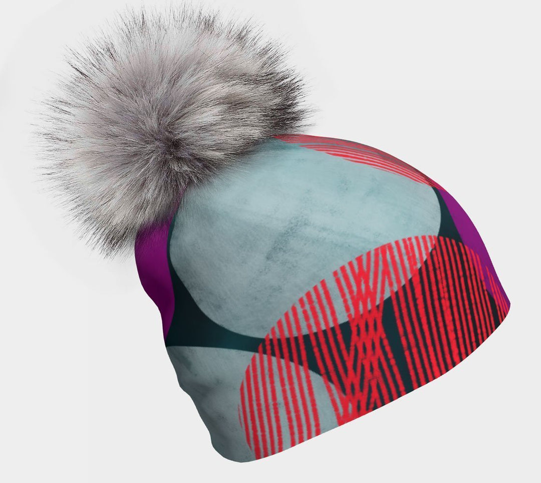 Teal-Dots Beanie with a grey fuzzy pompom against a dark background, showing abstract teal, red, and magenta circles.