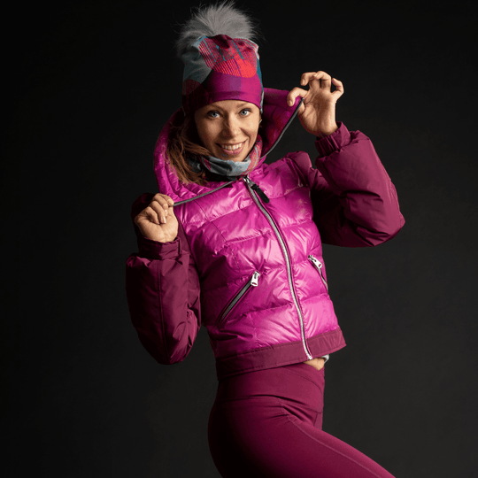 Woman posing in a bright pink winter jacket and leggings, adjusting the collar of her Teal-Dots Beanie and neck warmer.