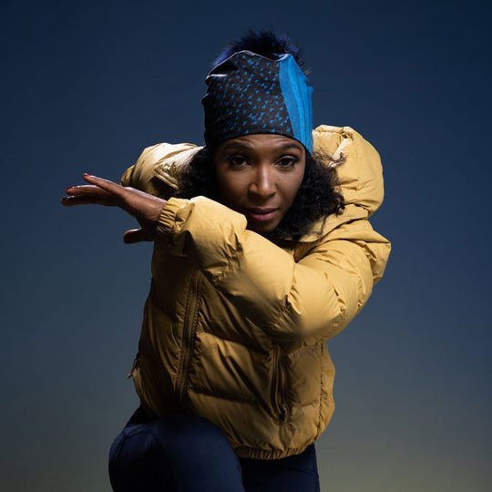 Woman wearing the Teal Flakes Beanie as a headband, showcasing its artful pattern with a yellow puffer jacket.