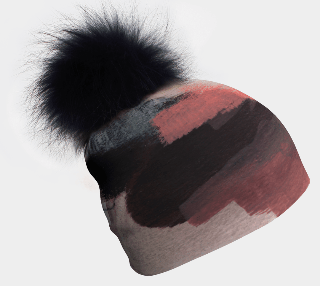 Beanie with a black pompom and abstract brushstroke pattern in coral, grey, and black.