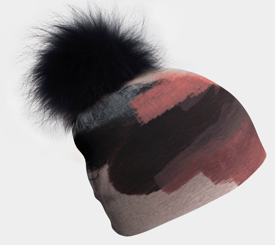 Beanie with a black pompom and abstract brushstroke pattern in coral, grey, and black.