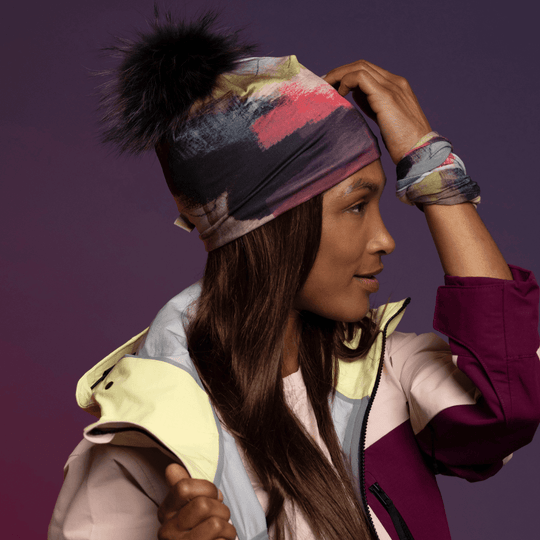 Side profile of a woman wearing the abstract art beanie and neck gaiter, touching her hair.