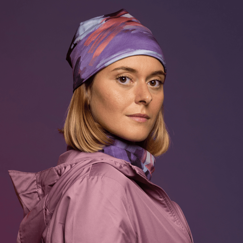 Woman wearing a purple abstract art pattern beanie and matching neck gaiter, with a pink jacket.