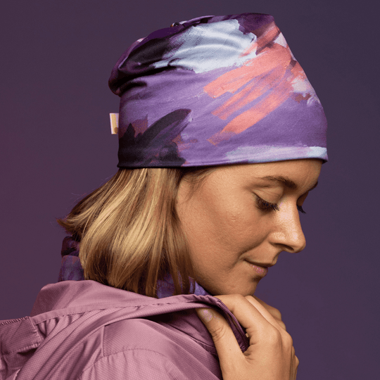 Woman wearing a purple abstract art pattern beanie and matching neck gaiter, with a pink jacket.