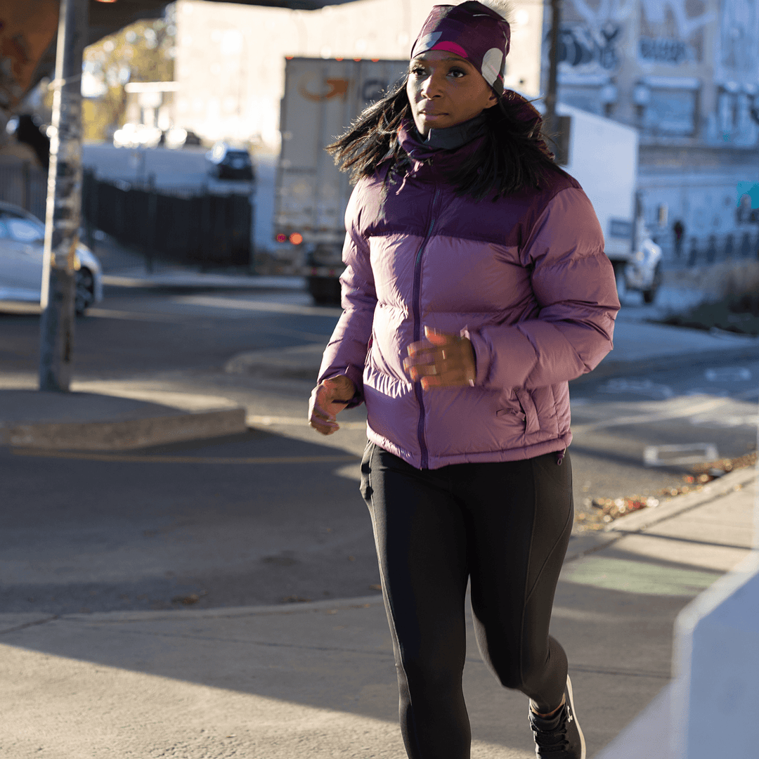 A woman running outdoors wearing a purple puffer jacket and the matching Umbrella Magenta Beanie.