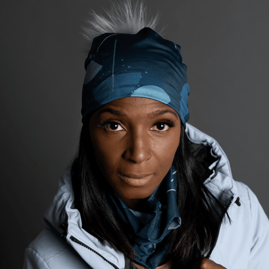 Close-up portrait of a woman wearing a teal beanie with a grey pompom and a matching neck warmer.