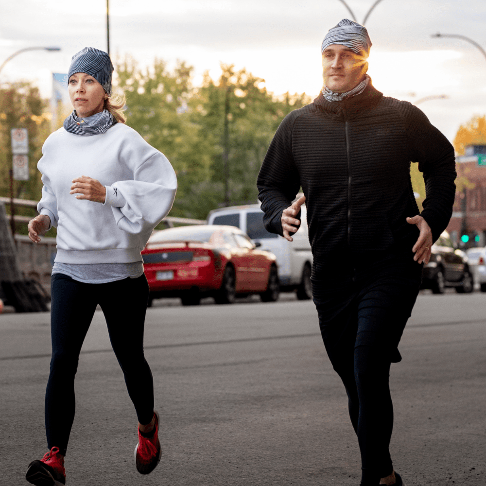 A man and woman running outdoors at sunset, both wearing the Abstract Lines Beanie and neck tubes.