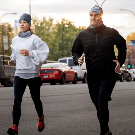 A man and woman running outdoors at sunset, both wearing the Abstract Lines Beanie and neck tubes.