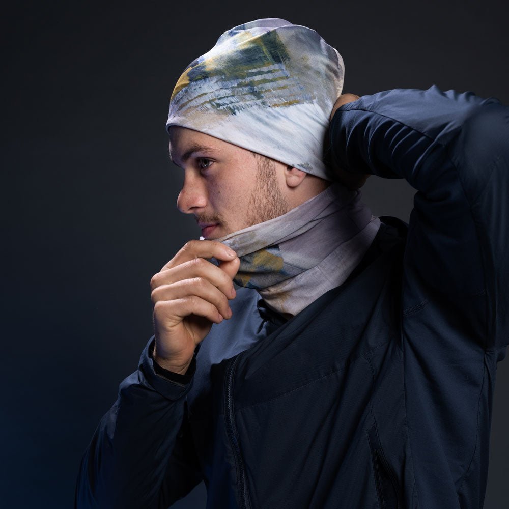 A man putting on the Unisex Sand Beanie while wearing a matching multifunctional neck tube.
