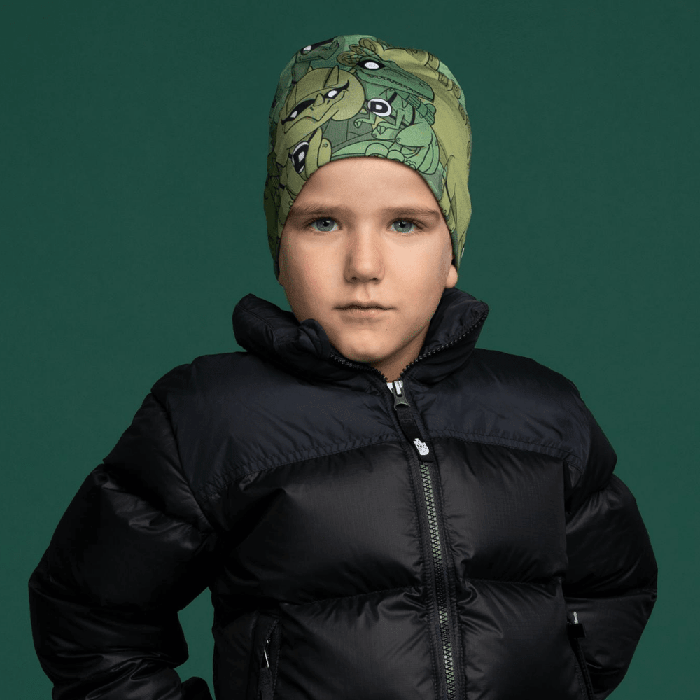 A young boy wearing the green dinosaur-themed beanie and a black puffer jacket.