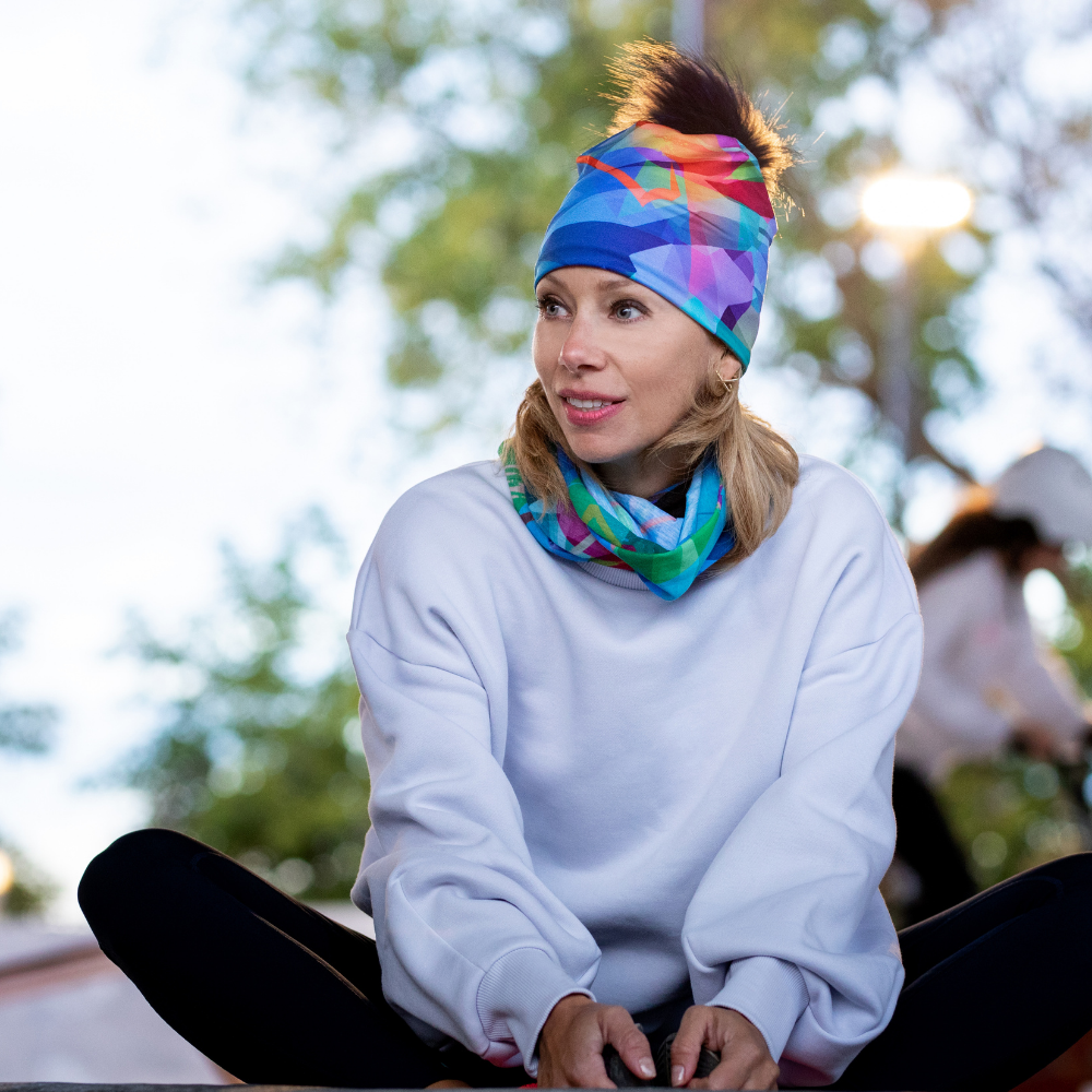 A woman wearing the Unisexe Fast Triangles Beanie with a matching neck tube while sitting outdoors in a relaxed pose.