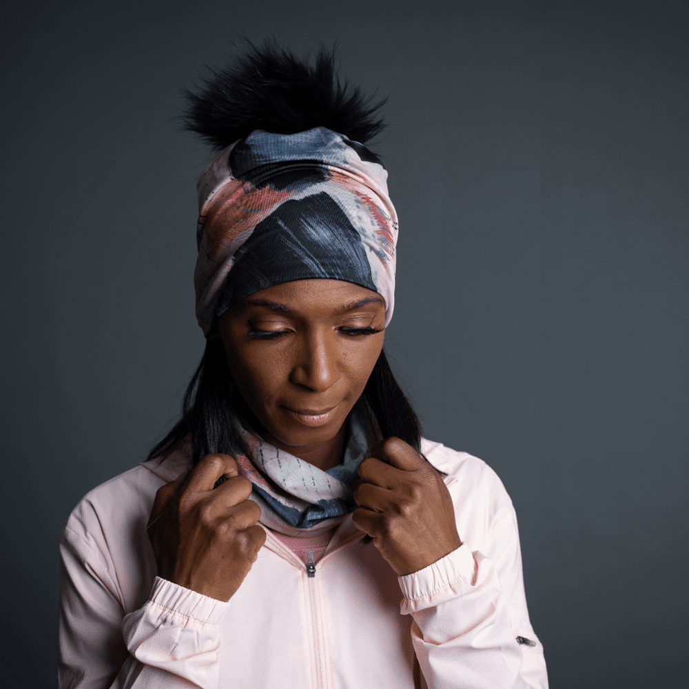 Woman wearing the Vie en Rose Beanie as a headband, with the black pompom visible, and adjusting a matching neck gaiter.