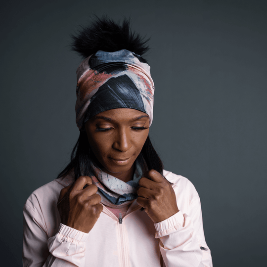 Woman wearing the Vie en Rose Beanie as a headband, with the black pompom visible, and adjusting a matching neck gaiter.