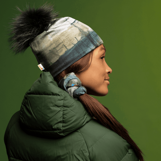 A woman wearing the Wall Beanie With Pompom and a green winter coat is shown in profile against a green background.