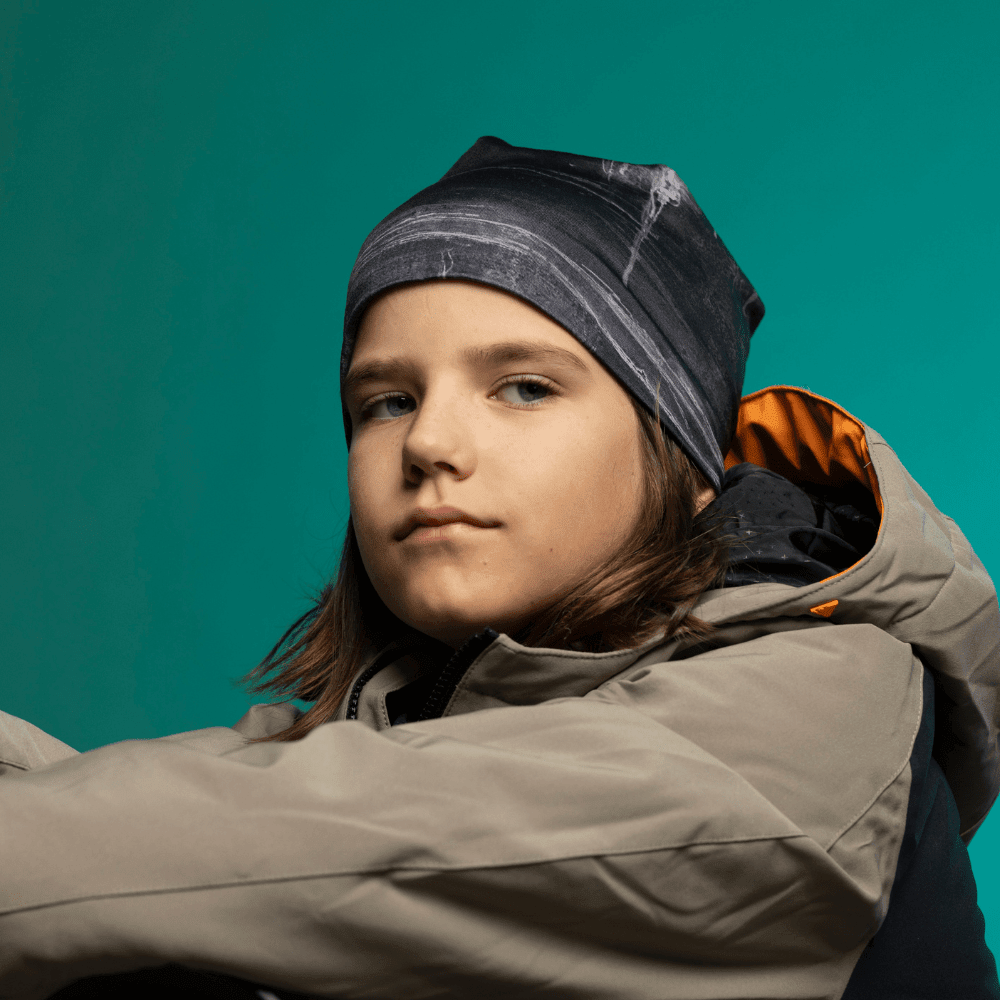 Child wearing the Wall Black Beanie with a grey and orange winter jacket against a teal studio background — close profile view