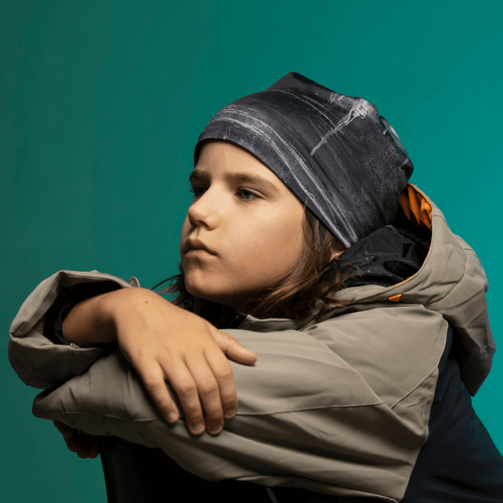 Child wearing the Wall Black Beanie in side profile, gazing away — full hat silhouette visible against teal background