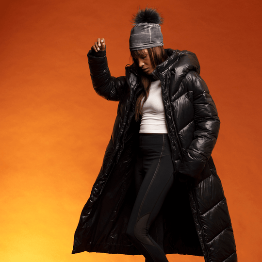 Woman in a long black puffer coat wearing a black art-print beanie with a pom-pom