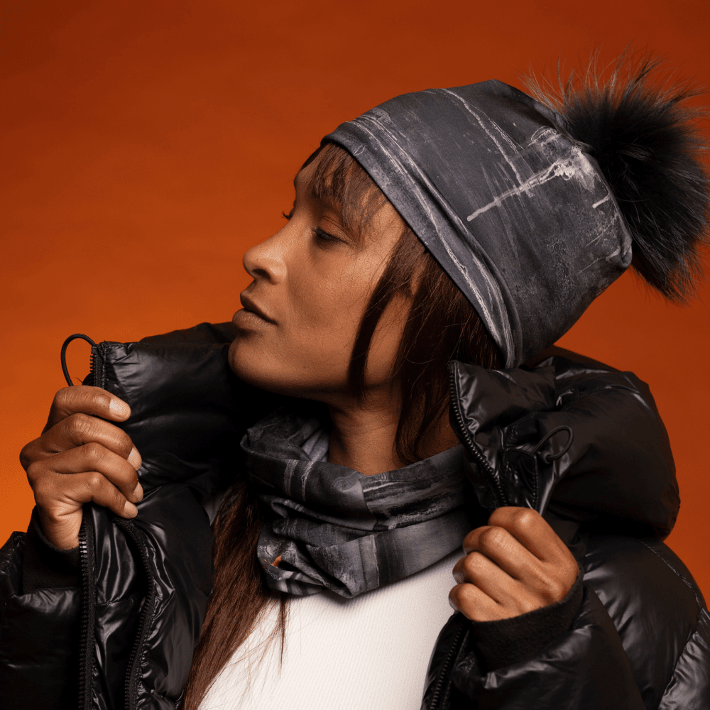 Woman in a black puffer coat wearing a black art-print beanie and scarf
