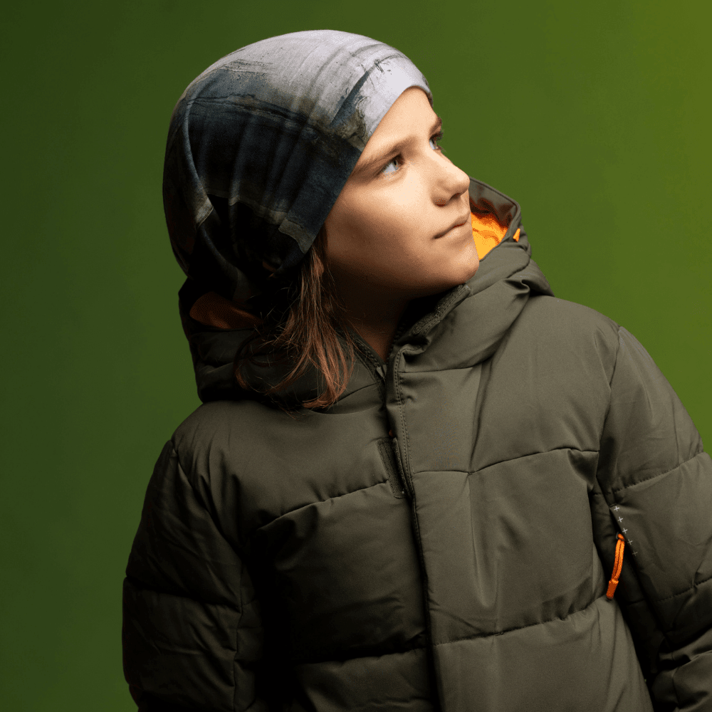 Young boy looking to the side, wearing the Wall Multifunctional Tube as a beanie with a green puffer jacket.
