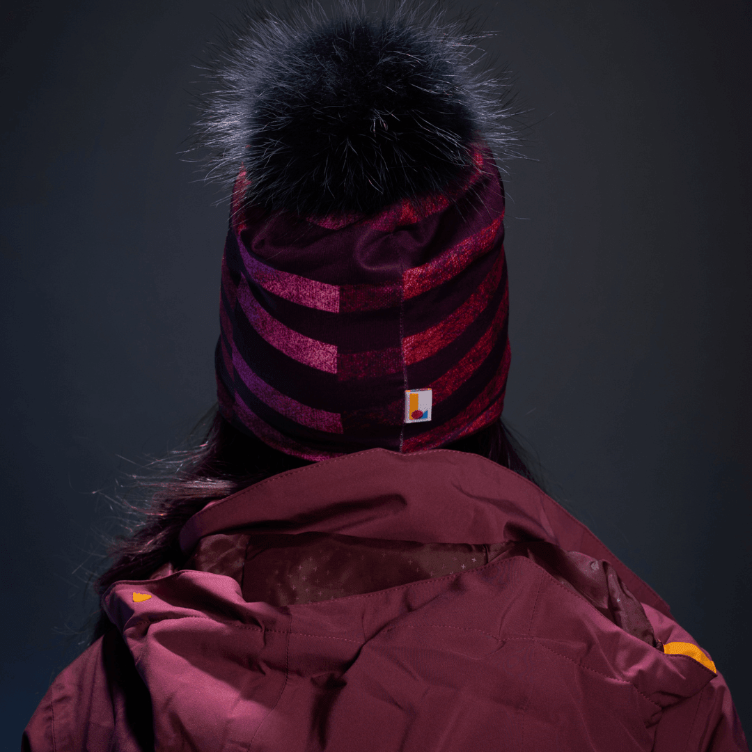 Back view of a woman wearing a purple and pink striped beanie with a black pom-pom.