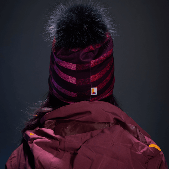 Back view of a woman wearing a purple and pink striped beanie with a black pom-pom.