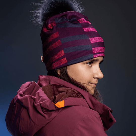 Woman wearing a purple and pink striped beanie with a black pom-pom, looking to the side.